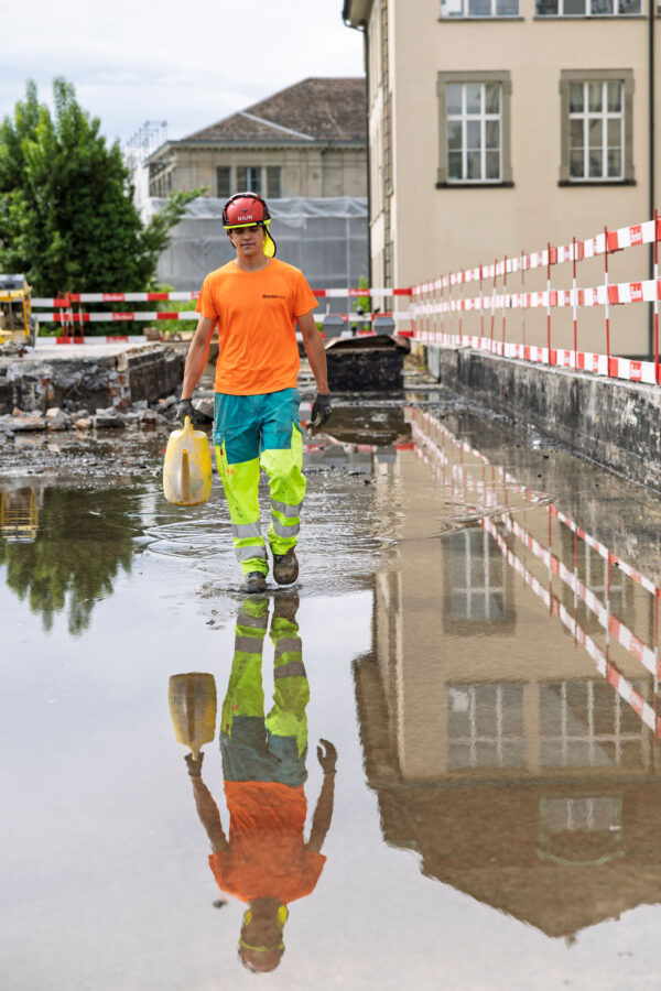 Bauarbeiter mit Giesskanne watet durch Wasserlache
