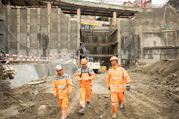 Drei Bauarbeiter in der Baugrube FORUM UZH vor Bohrpfahlwand und Spriessungen