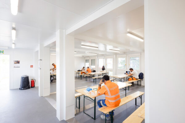 Aufenthaltsraum mit Bauarbeitenden in orangefarbener Arbeitskleidung