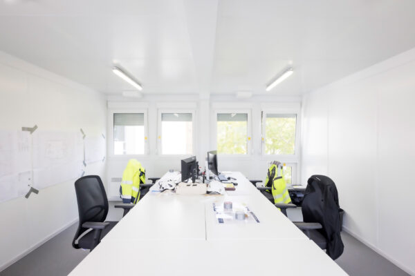 Baustellenbüro mit grossem Sitzungstisch, neongelben Jacken und Bildschirmen