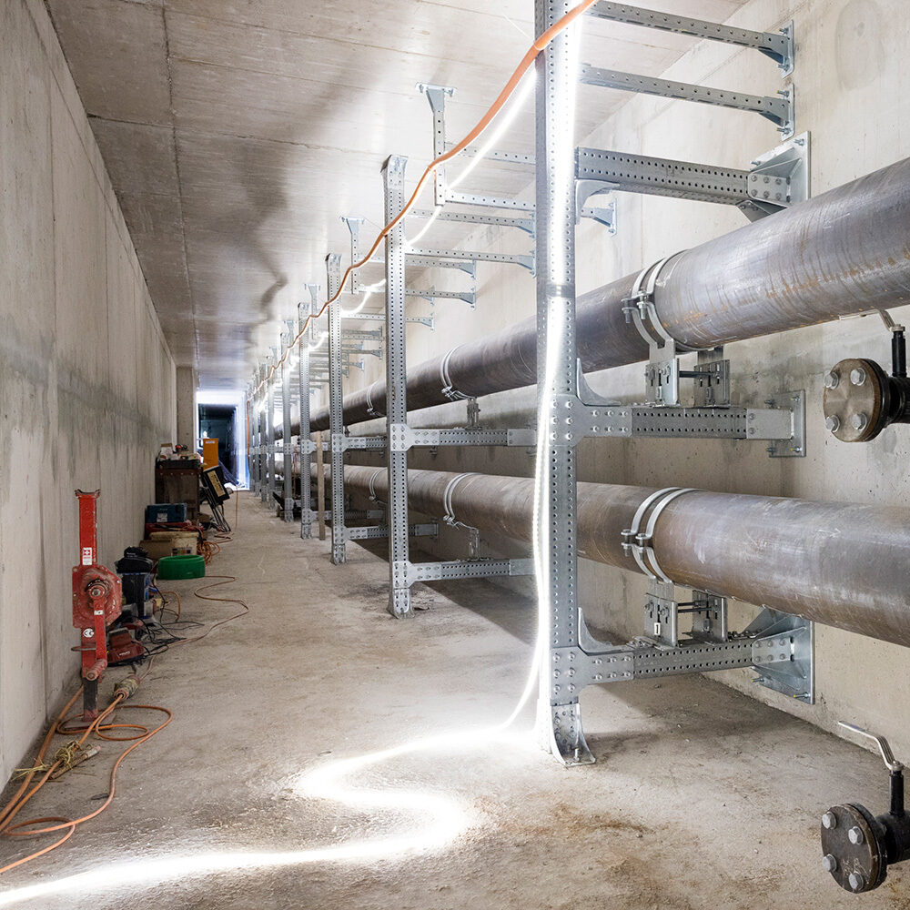 Fernwärmerohre im begehbaren Fernwärmekanal, montiert auf Metallträgern entlang der Betonwand.
