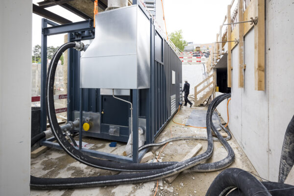 Ansicht des Fernwärmekanals auf der Baustelle mit angeschlossenen Leitungen und technischem Container.