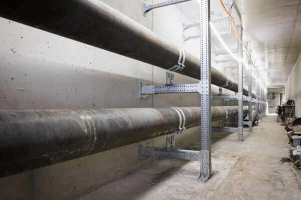 Fernwärmekanal mit parallel verlaufenden Fernwärmerohren auf Metallkonstruktionen entlang der Betonwand.