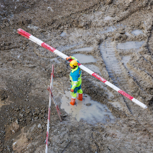 Bauarbeiter mit Absperrstange auf der Schulter im schlammigen Baugrund
