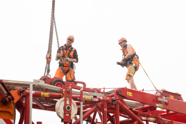 Zwei Bauarbeiter sichern ein Turmsegment eines Turmdrehkrans während der Montage.