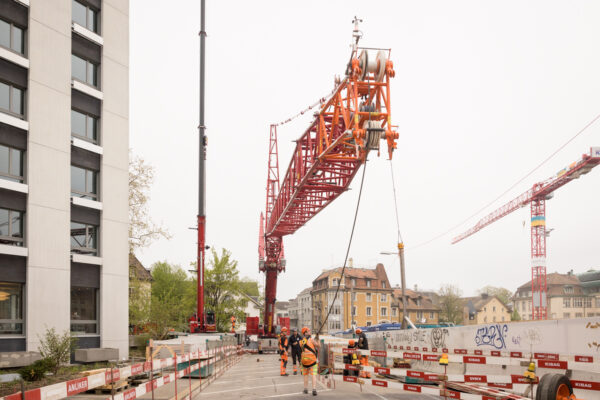 Pneukran hebt den Kranarm eines Turmdrehkrans über eine abgesperrte Strasse.