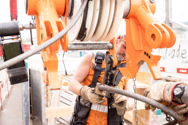 Bauarbeiter befestigt ein Stahlseil an der Lastaufnahme eines Kranelements.