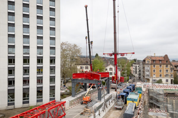 Zwei Pneukrane heben eine Stahlkonstruktion für ein Portal auf der FORUM UZH-Baustelle an.