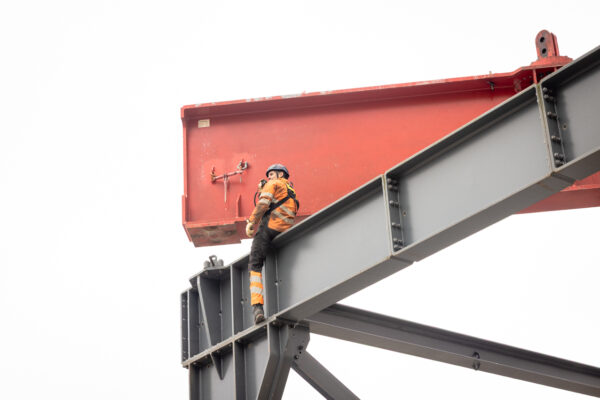 Bauarbeiter sitzt auf einem Stahlträger und begleitet die Montage eines Portalbauteils.